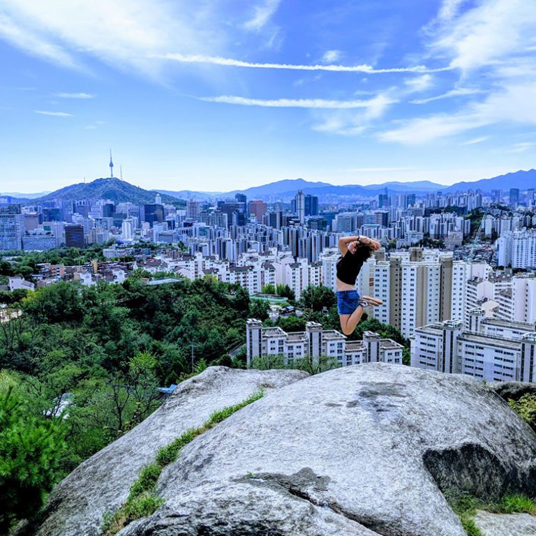 Digital nomad jumps into the air after hiking mountain in Seoul, Korea with view of Namsan Tower