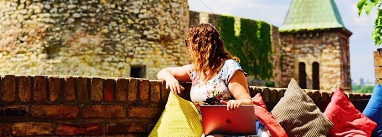 Girl Working on her laptop in Belgrade with a view of a castle in the background