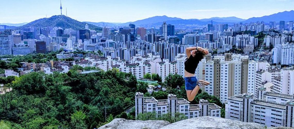 Digital nomad jumps into the air after hiking mountain in Seoul, Korea with view of Namsan Tower